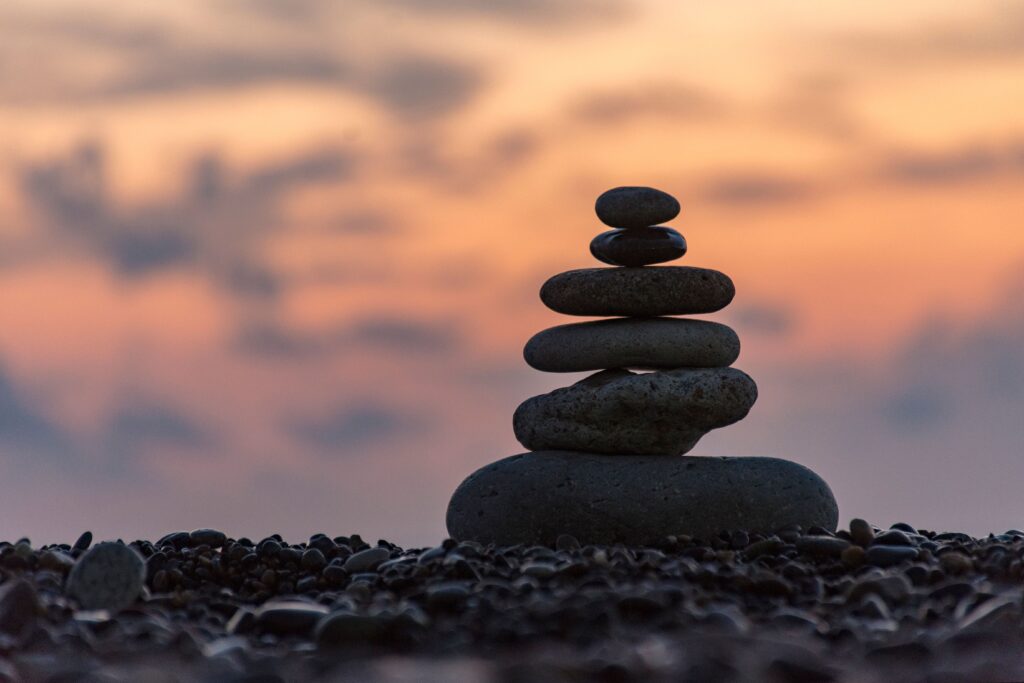Balanced stack of smooth stones near water during sunset representing emotional stability, calmness, and mindfulness.