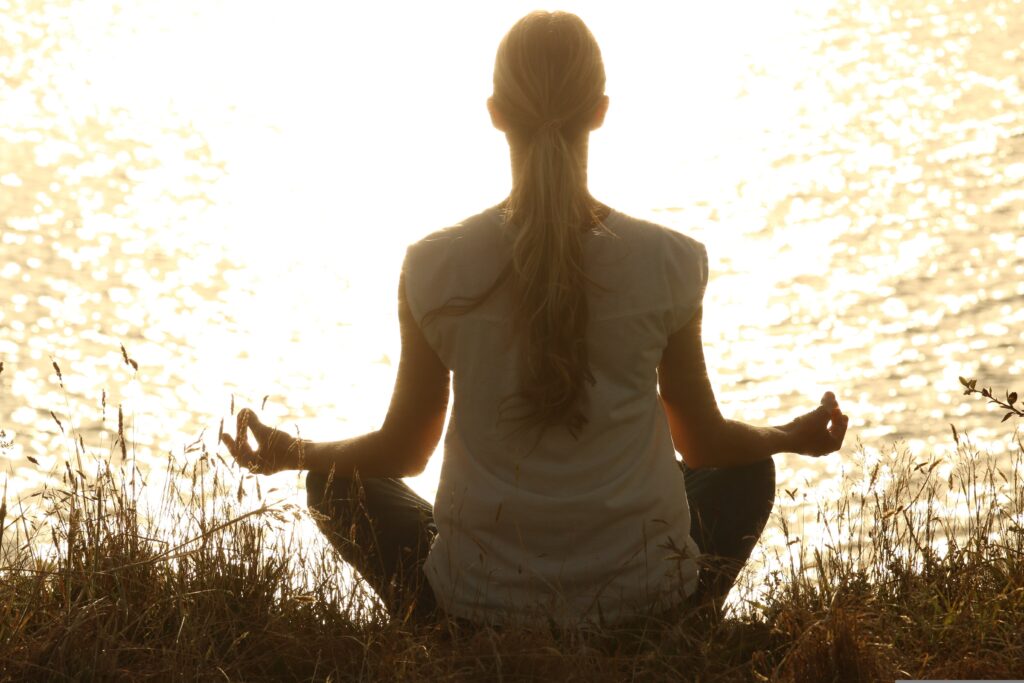 Person meditating near a glowing lake during sunrise, symbolizing mindfulness, inner peace, and spiritual balance.